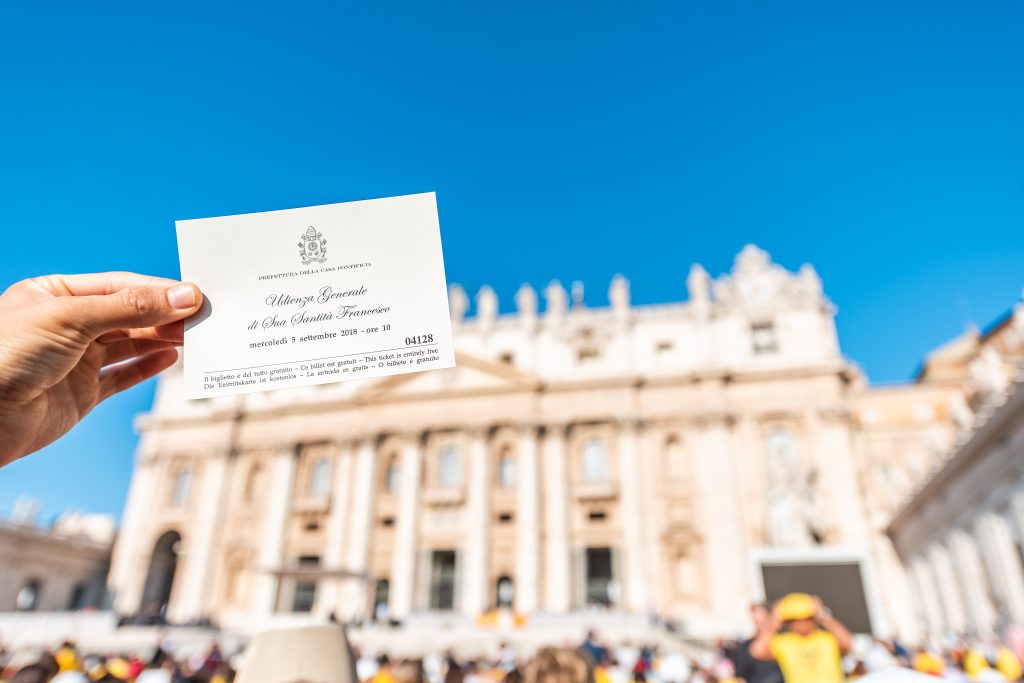 Vatican City, Italy - September 5, 2018: Closeup of hands holding admission ticket for church in St Peter's Square Basilica during mass, papal audience on sunny day, Rome